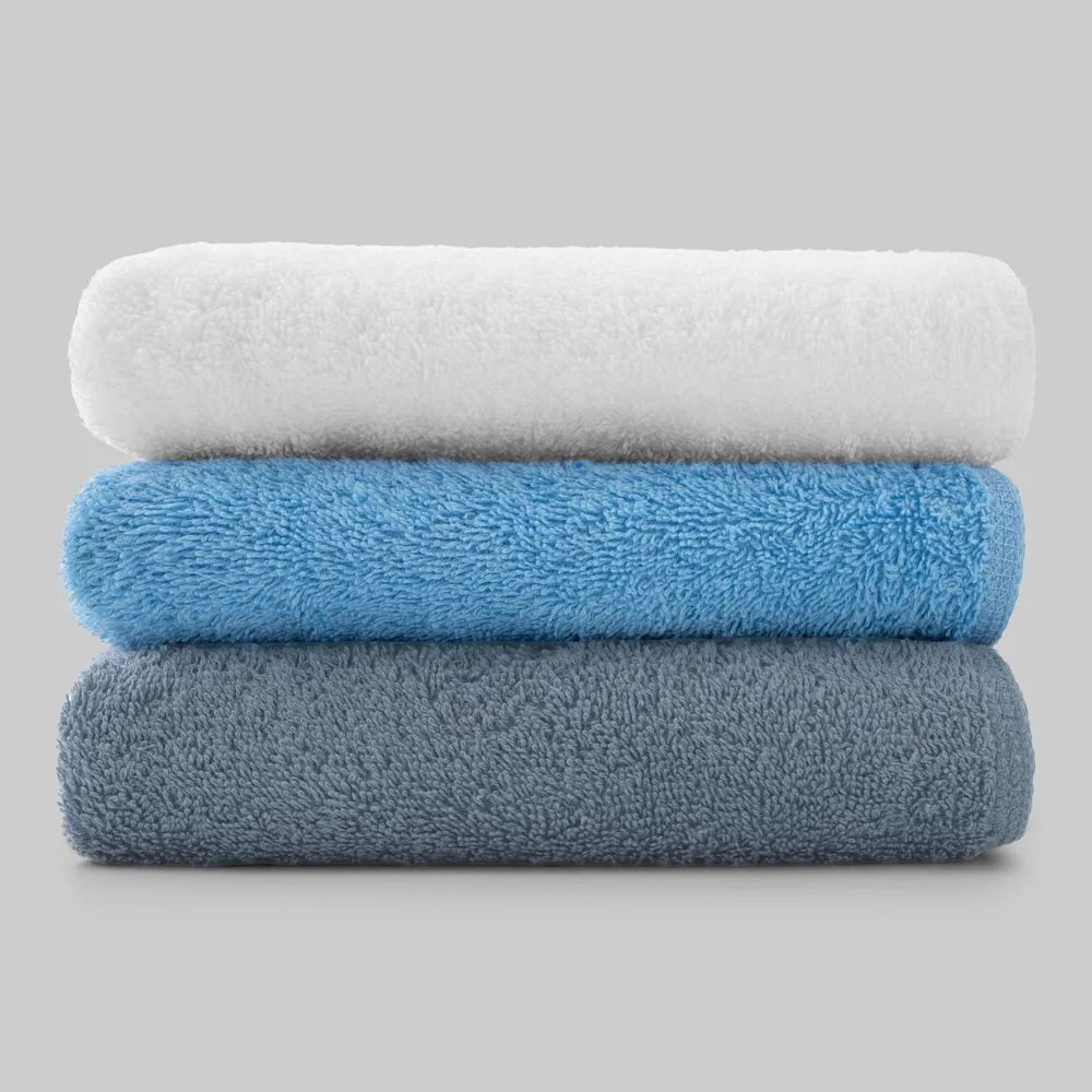 Ba chiếc khăn tắm xếp chồng chụp nền trắng, ánh sáng chếch làm lộ rõ kết cấu sợi bông